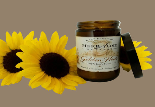An amber glass jar of Herb Alzise Butters Golden Flour triple body butter with its black lid leaning against it, styled with three yellow sunflowers on a clean white background.