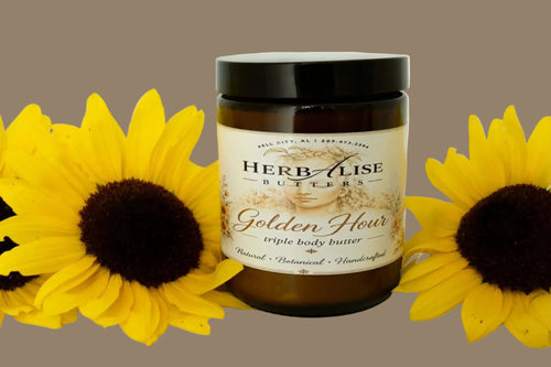 A jar of Herbalise Butters Golden Hour triple body butter, styled with two yellow sunflowers on either side against a plain white background.